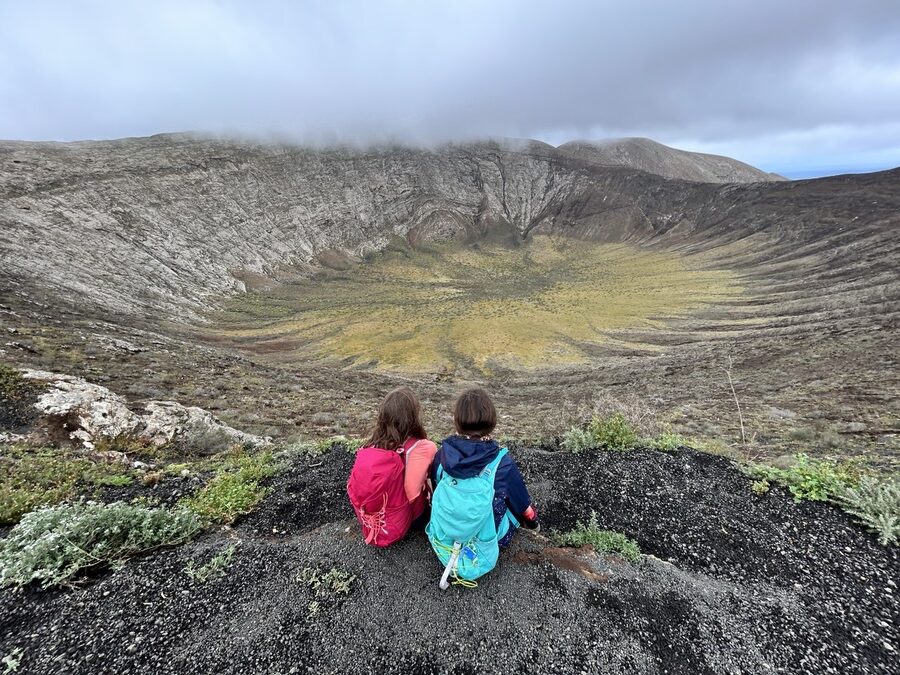 Deux enfants assis dans la nature, sacs à dos sur les épaules, face à un paysage de montagne
